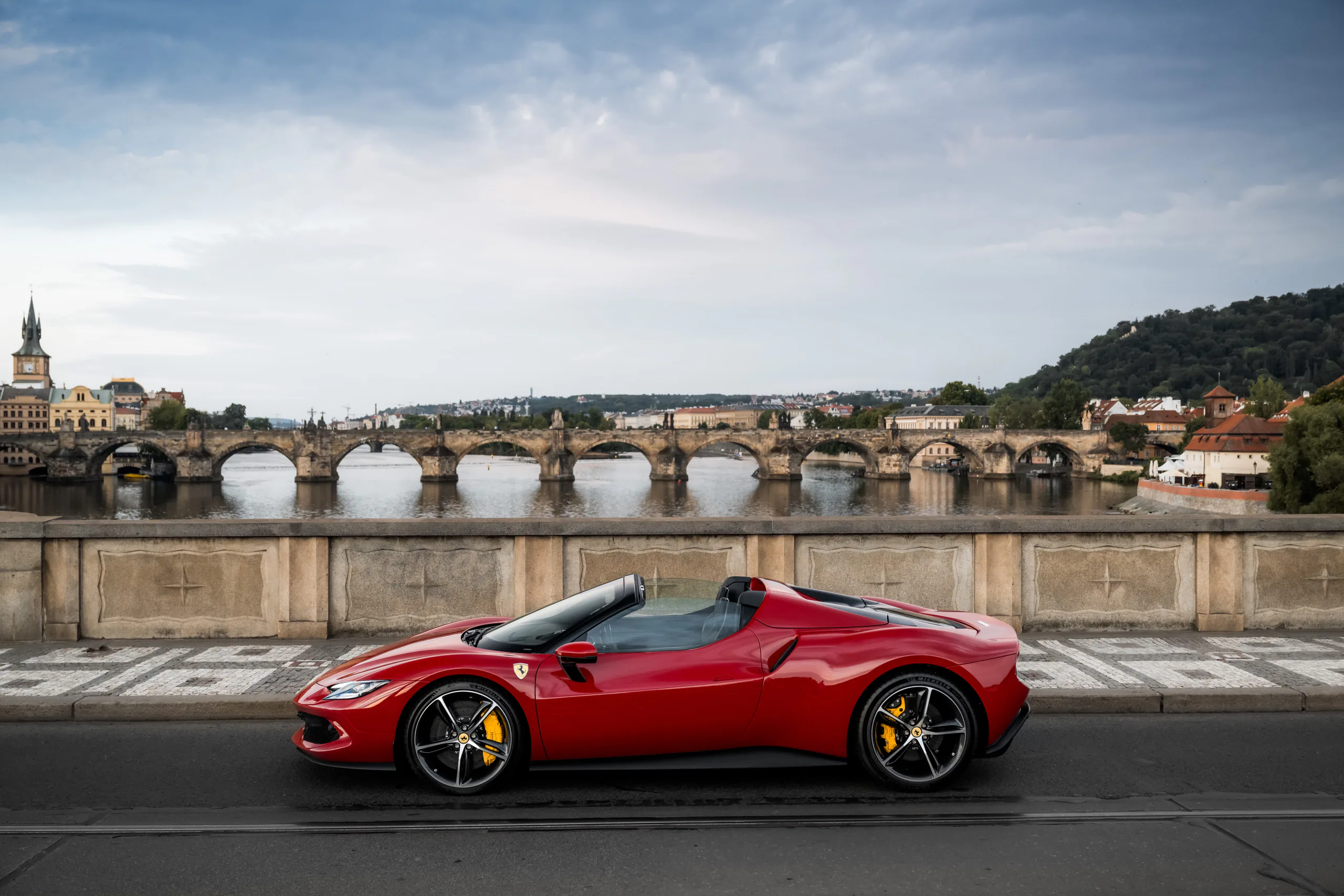 Red Ferrari 296 GTS in profile with Charles Bridge and the Vltava behind